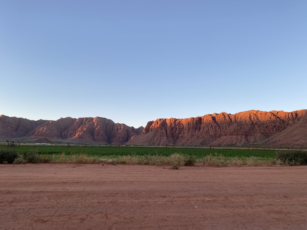 Desert red mountains at sunrise with green field