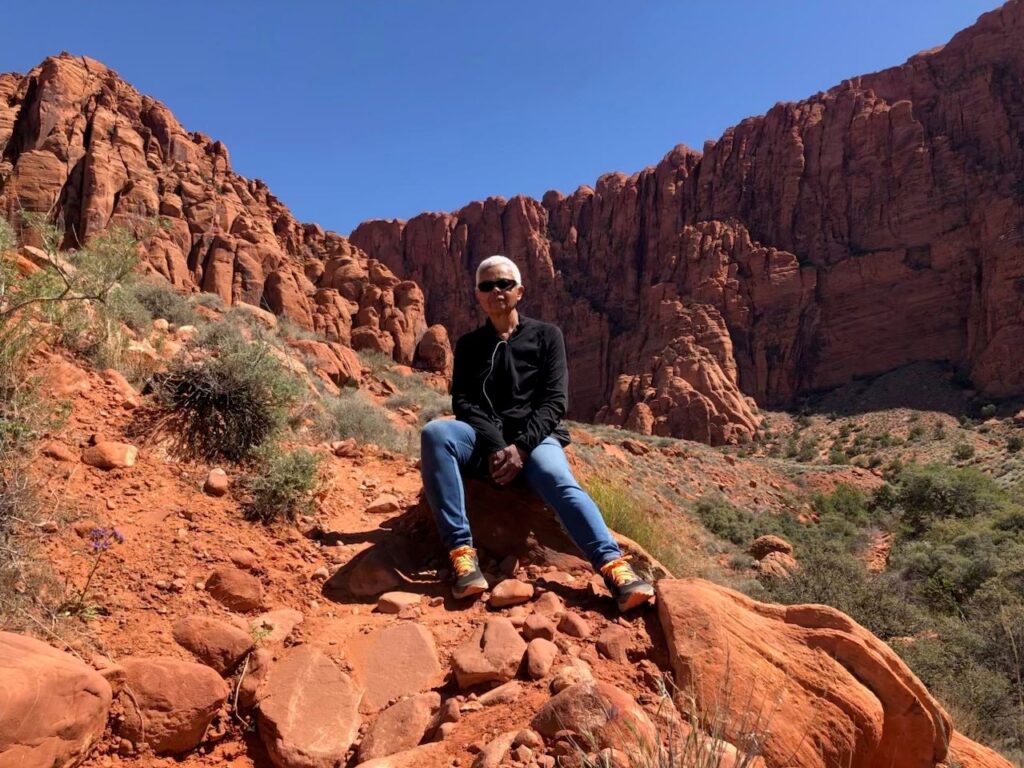 Picture of carole richard sitting on a pile of red rocks in a desert canyon