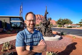 Dave hererro wearing a blue shirt standing in front of a statue in the southwest desert